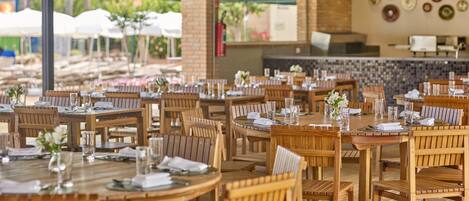 A restaurant with wooden tables and chairs, arranged in a spacious outdoor setting with brick walls and a tiled floor.