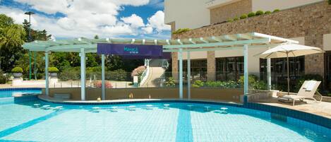 Una piscina con zona cubierta, un cartel que dice "Manac" y un edificio de fachada de piedra y vegetación.