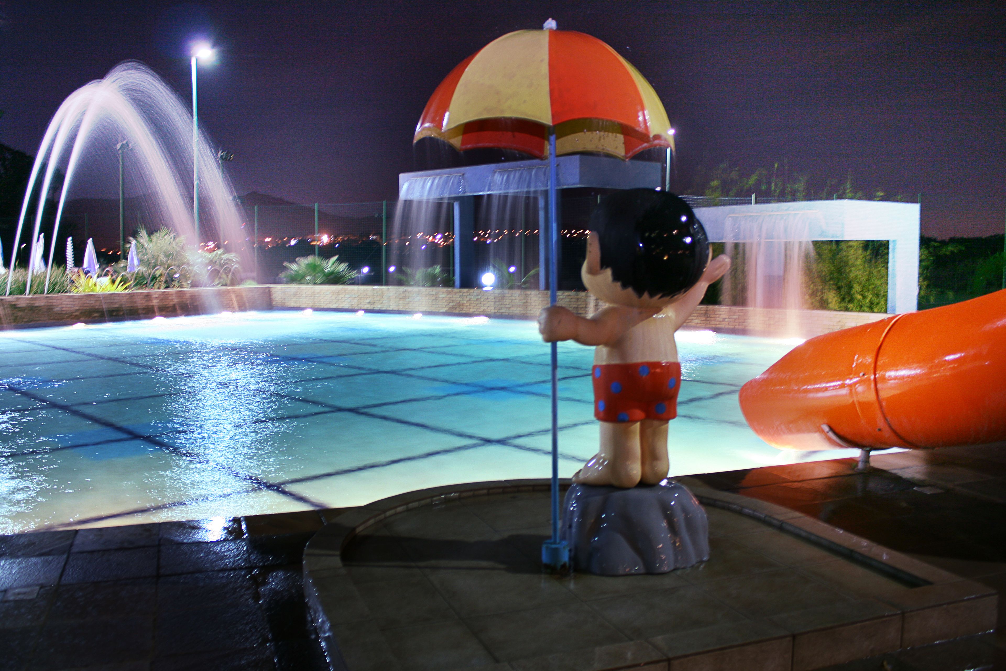 A water park with a water fountain, a water slide, and a covered area with a dome.