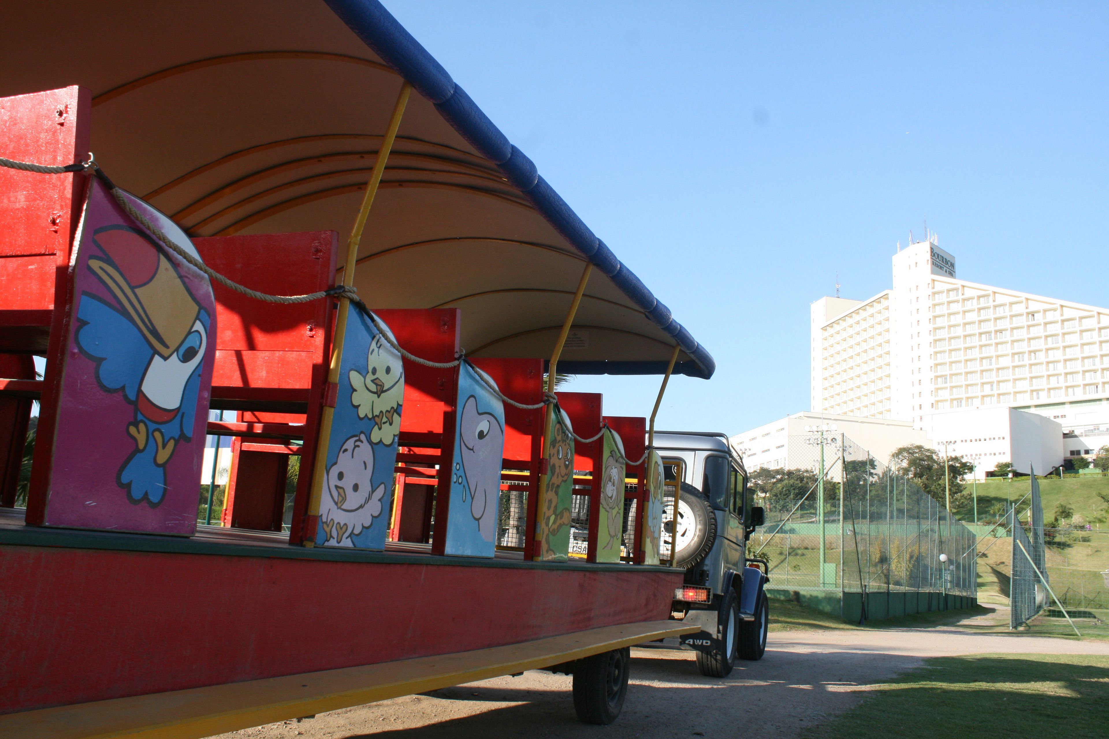 Ein farbenfrohes Kinderfahrgeschäft mit Zeichentrickfiguren, einem überdachten Sitzbereich und einem bereitstehenden Fahrzeug.