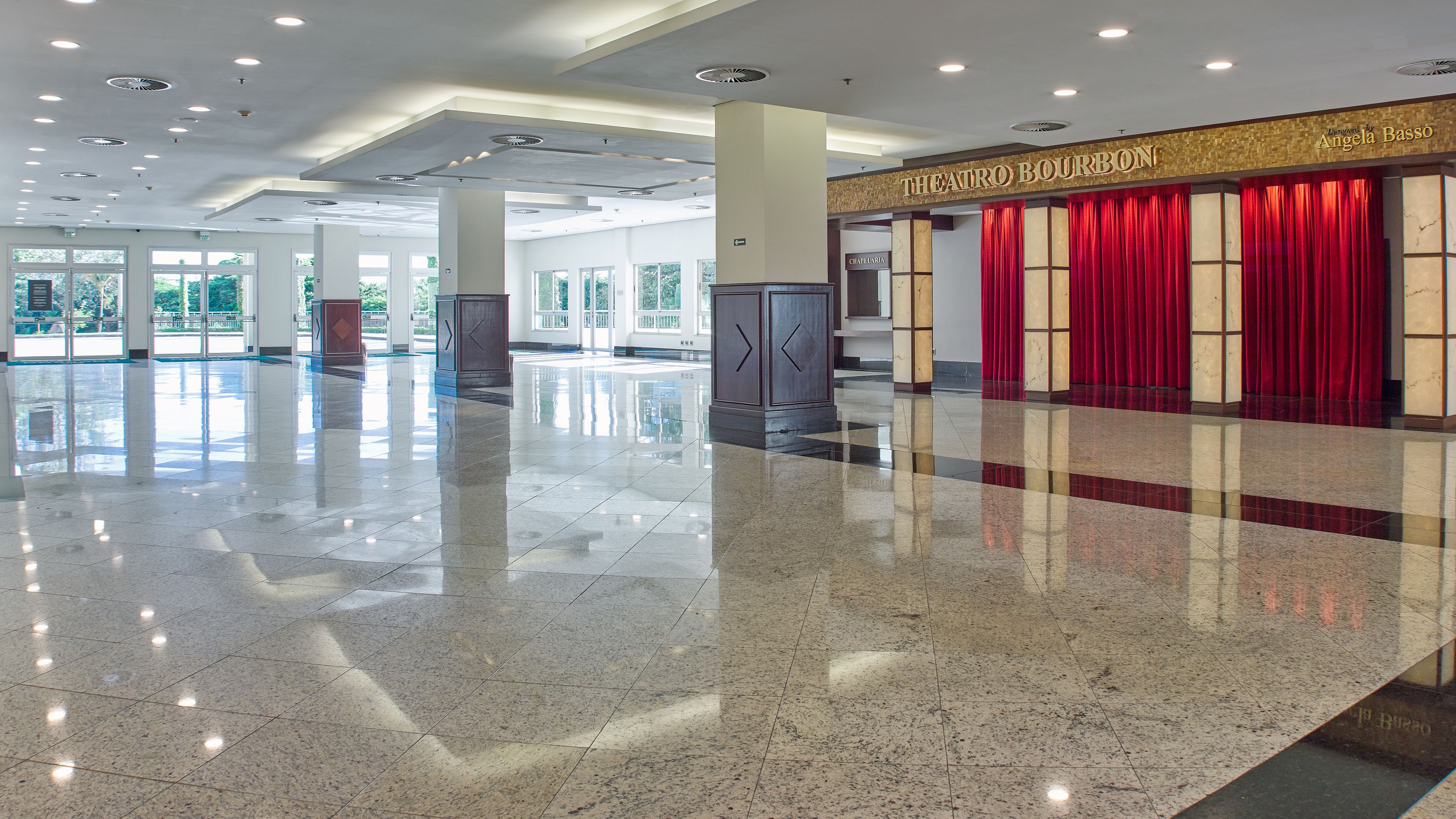 A spacious lobby with a polished marble floor, a grand staircase, and a theater area with red curtains.