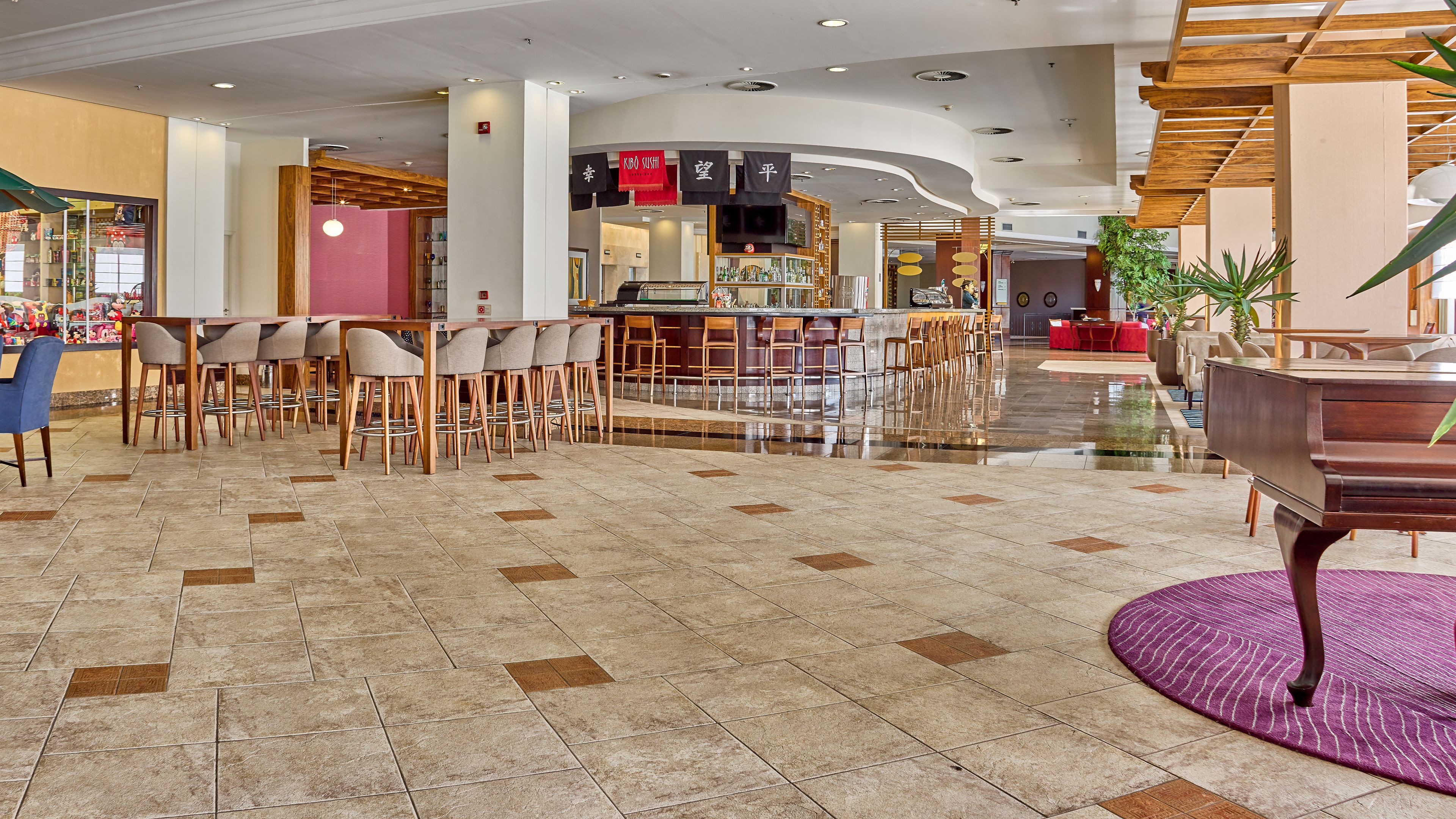 A modern lobby with a bar area, seating arrangements, and a piano.