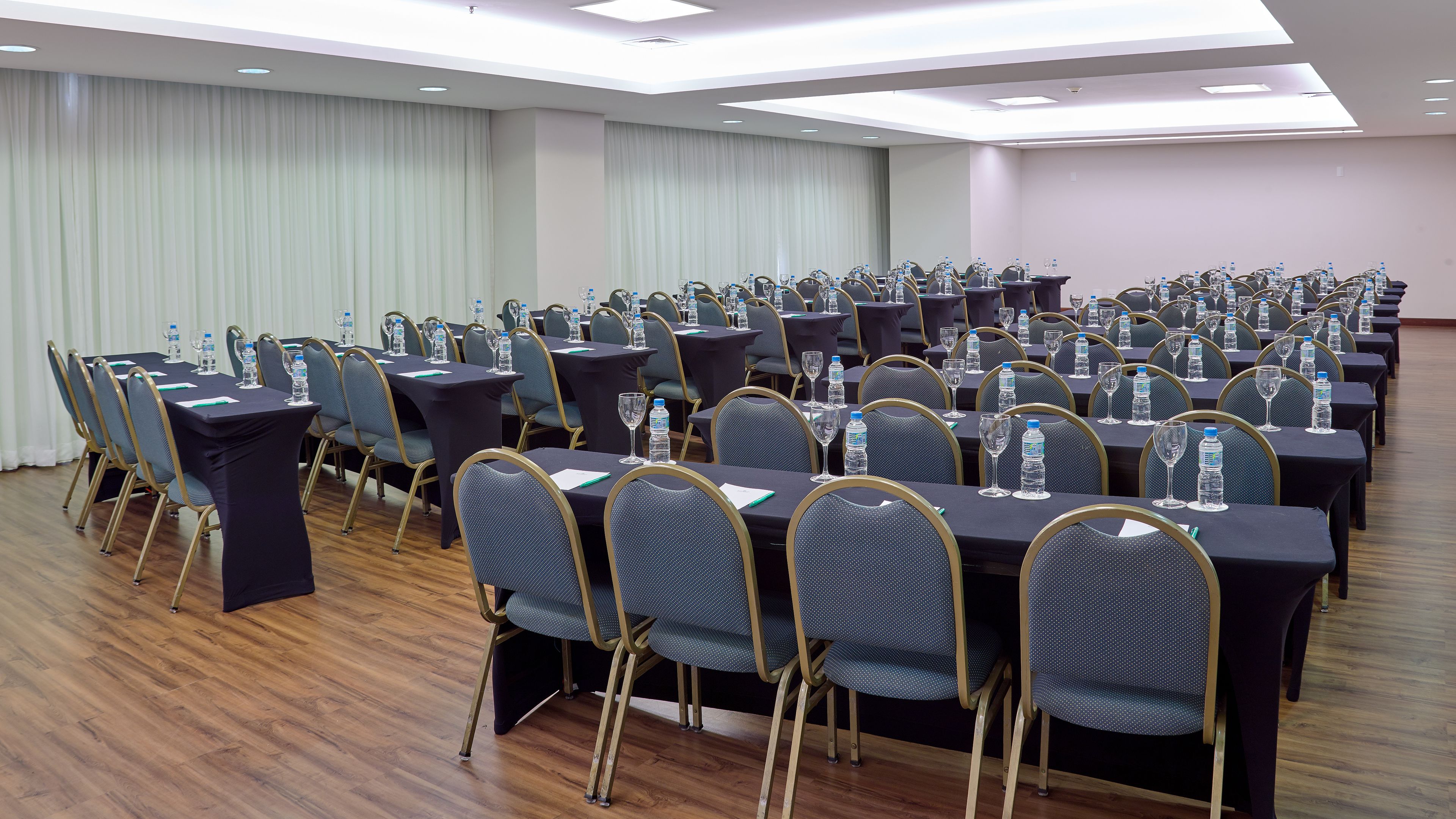 A conference room with rows of tables and chairs, equipped with water bottles and glasses.