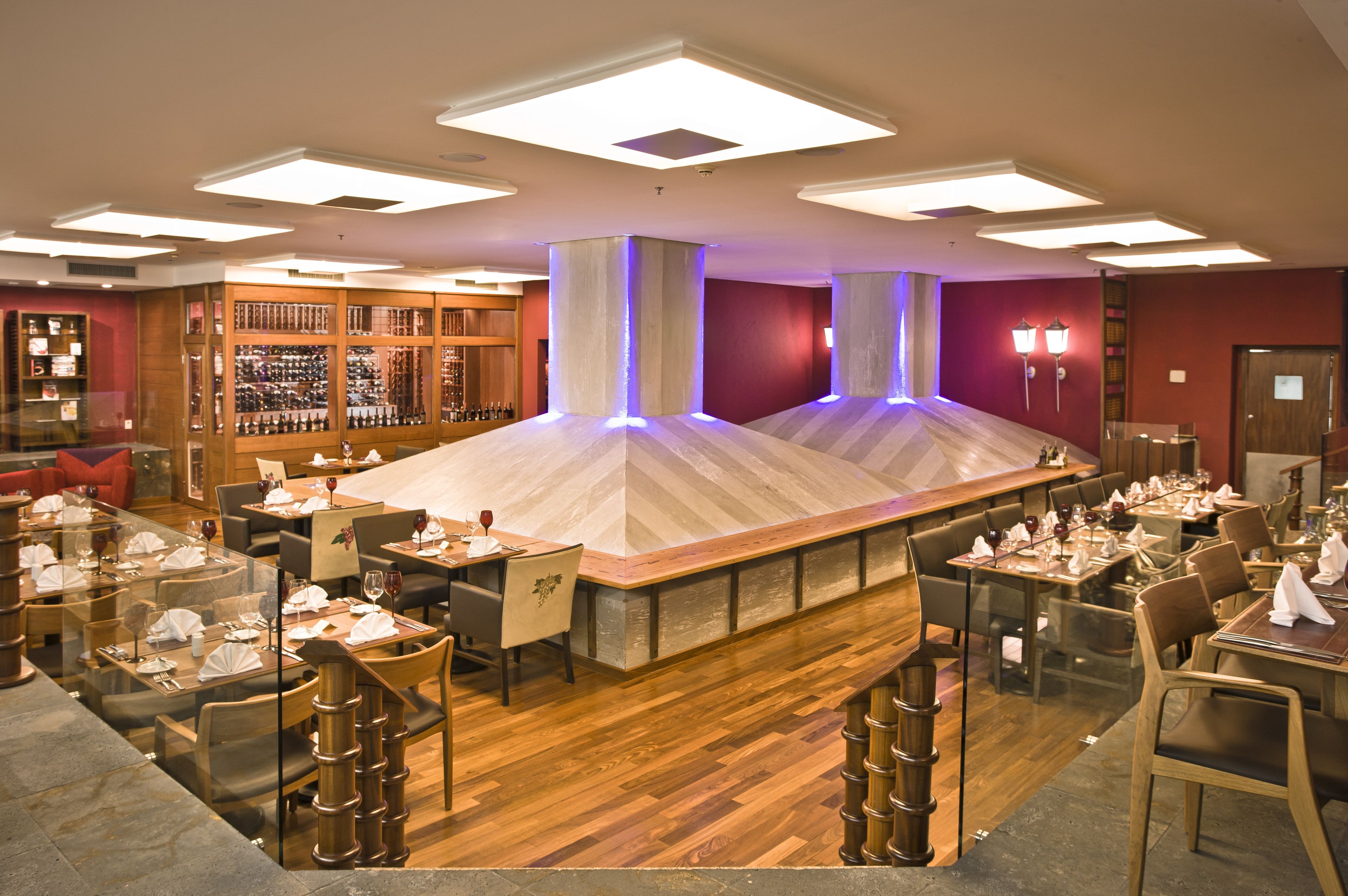 A restaurant with a central bar area, multiple dining tables, and a wine display.