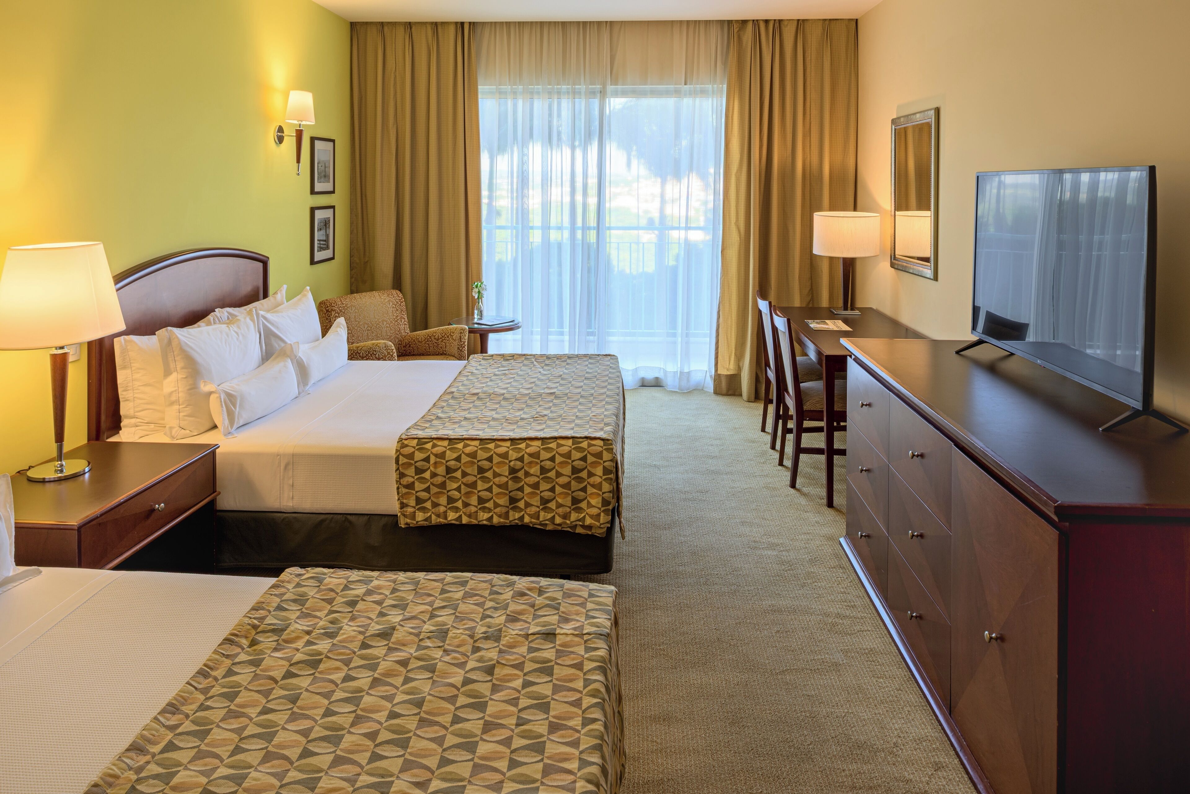 A hotel room with two beds, a TV, a desk, and a window with curtains.
