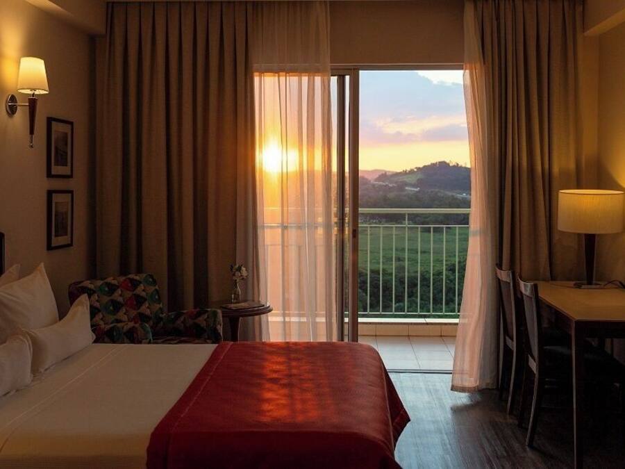 Habitación de hotel con cama, escritorio, silla, lámpara y vista al atardecer a través de la ventana.