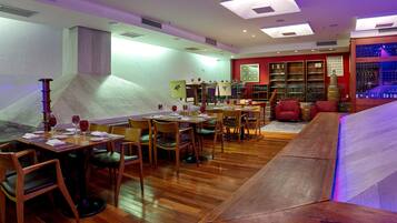 A restaurant with wooden tables and chairs, a wine rack, and a red armchair.