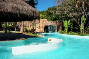 Une piscine dotée d’une structure à toit de chaume, d’une cascade et d’une végétation luxuriante.