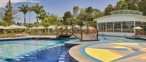 Una piscina con un puente, sillas de descanso y sombrillas.