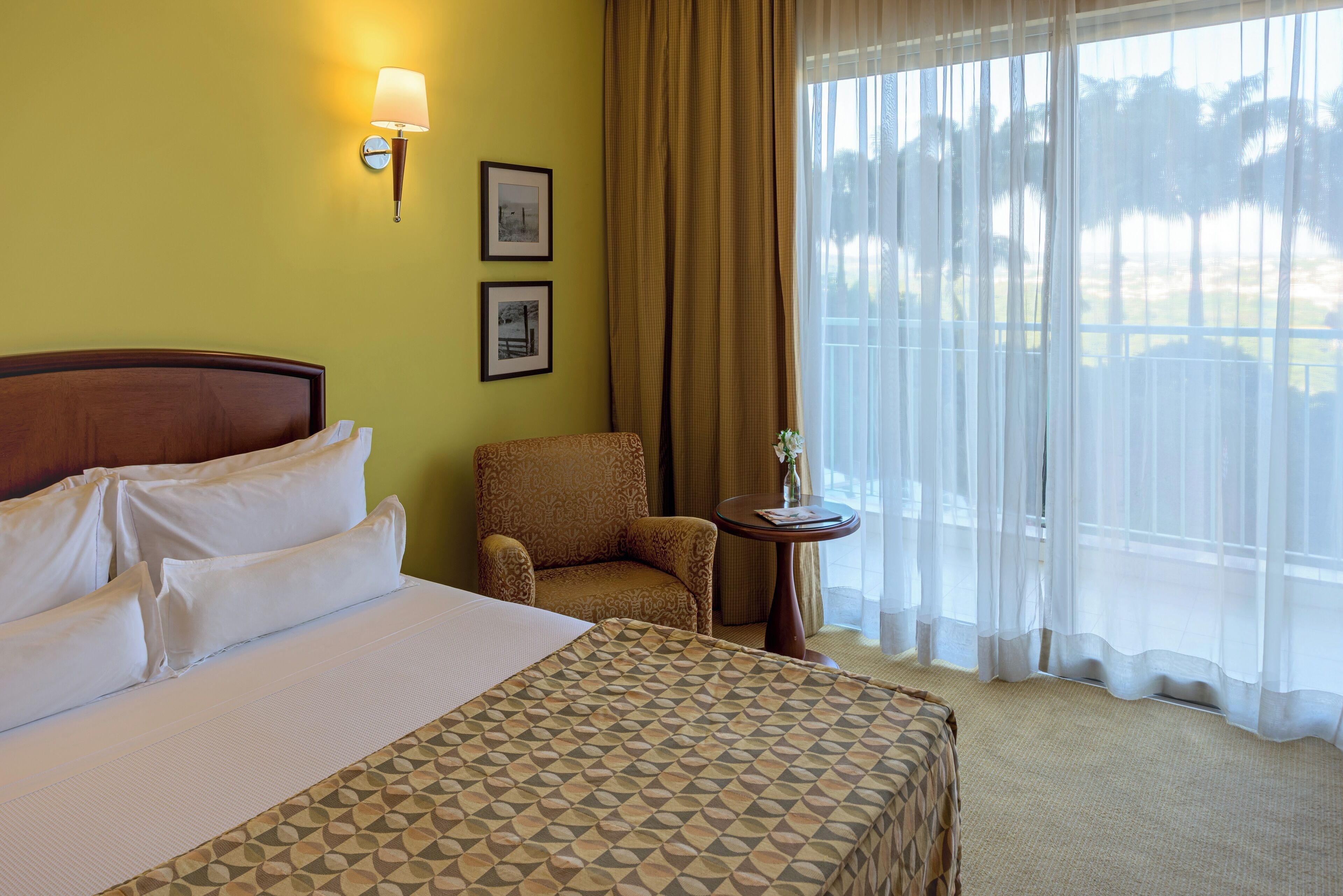 A hotel room with a large bed, a chair, a small table, and a window with curtains.
