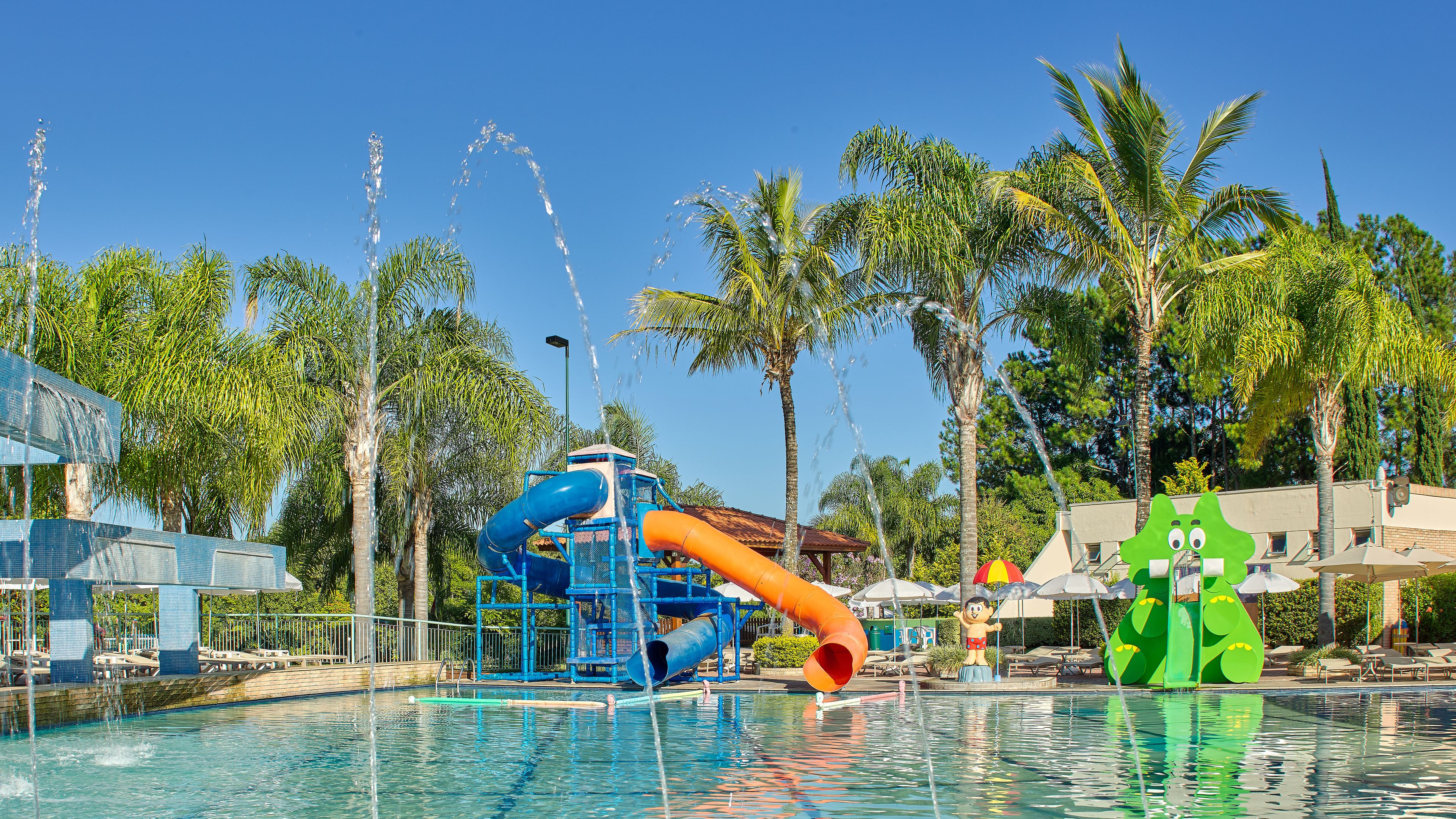 Parque acuático con un tobogán de agua azul, piscina y palmeras.