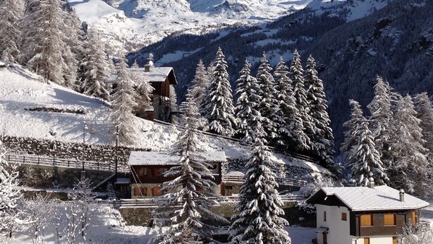 A snow-covered mountain village with traditional wooden buildings, a ski lift, and a clear view of the surrounding peaks.