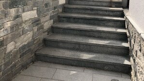 A stone staircase leading to a building entrance, with a wooden handrail and a sign indicating 'BUDAPEST ROOMS'.