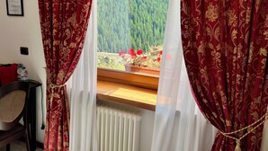 A room with a window featuring red curtains with a gold pattern, a radiator below, and a chair to the left.