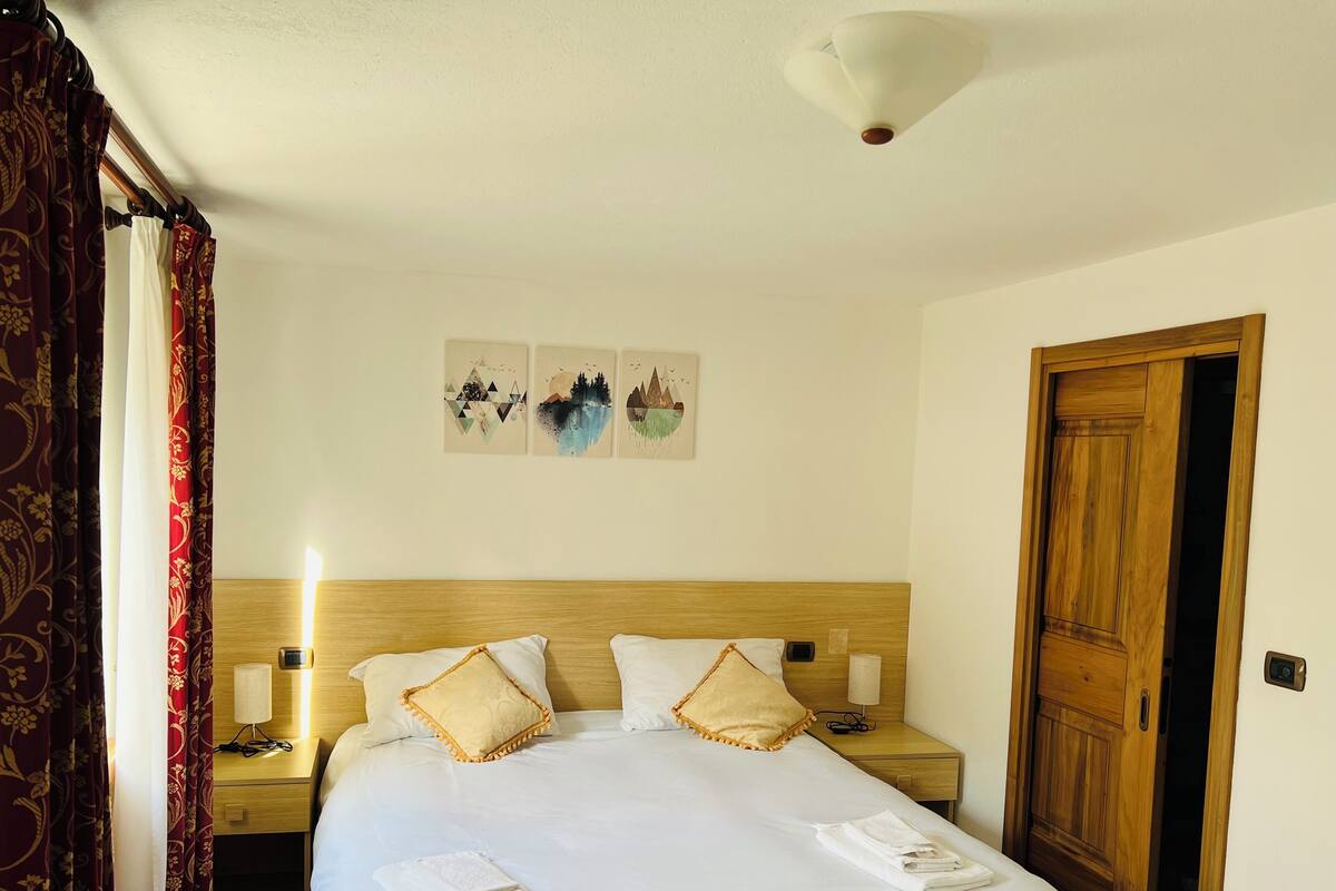 Ett hotellrum med en sänggavel i trä, två sängbord, en säng med vita sängkläder, en nattlampa och en dörr.