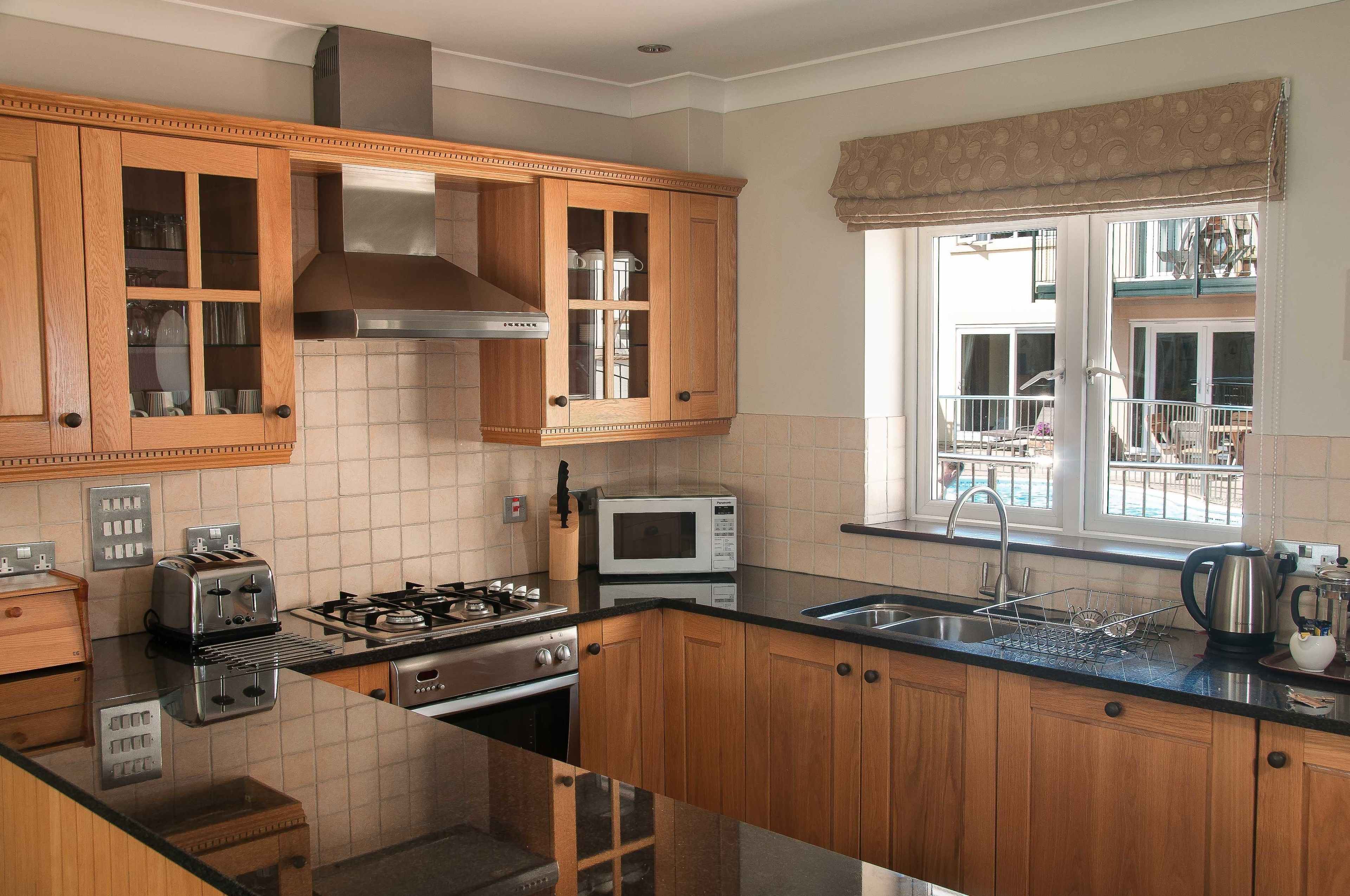 A kitchen with wooden cabinets, a stainless steel range hood, a microwave, a gas stove, and a window with a view of the outside.