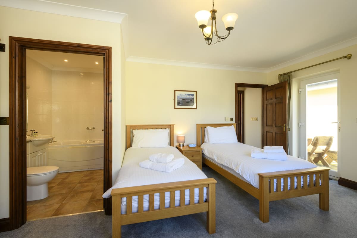 A hotel room with two wooden beds, a bathroom with a bathtub, and a chandelier.