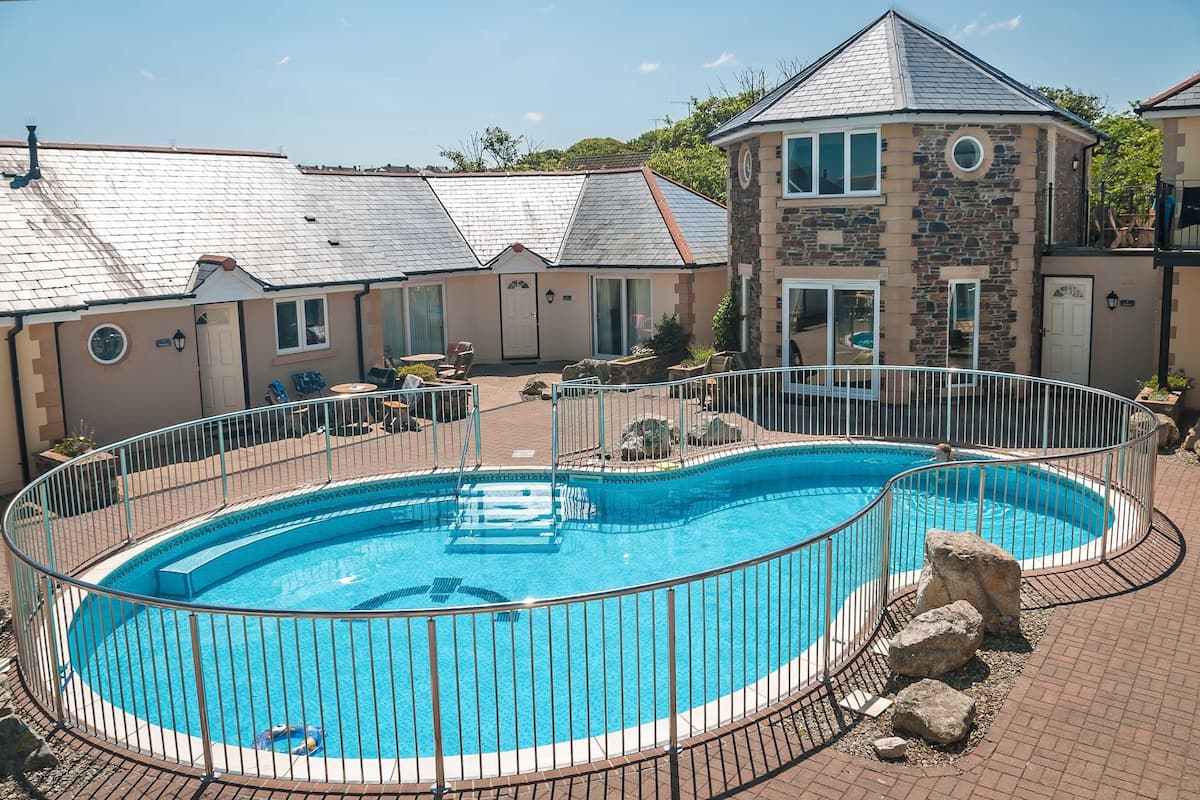 A swimming pool with a metal fence, surrounded by a brick patio.