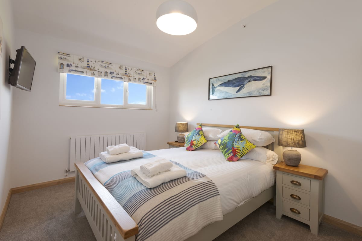 A bedroom with a bed, bedside tables, a window, and a wall-mounted TV.