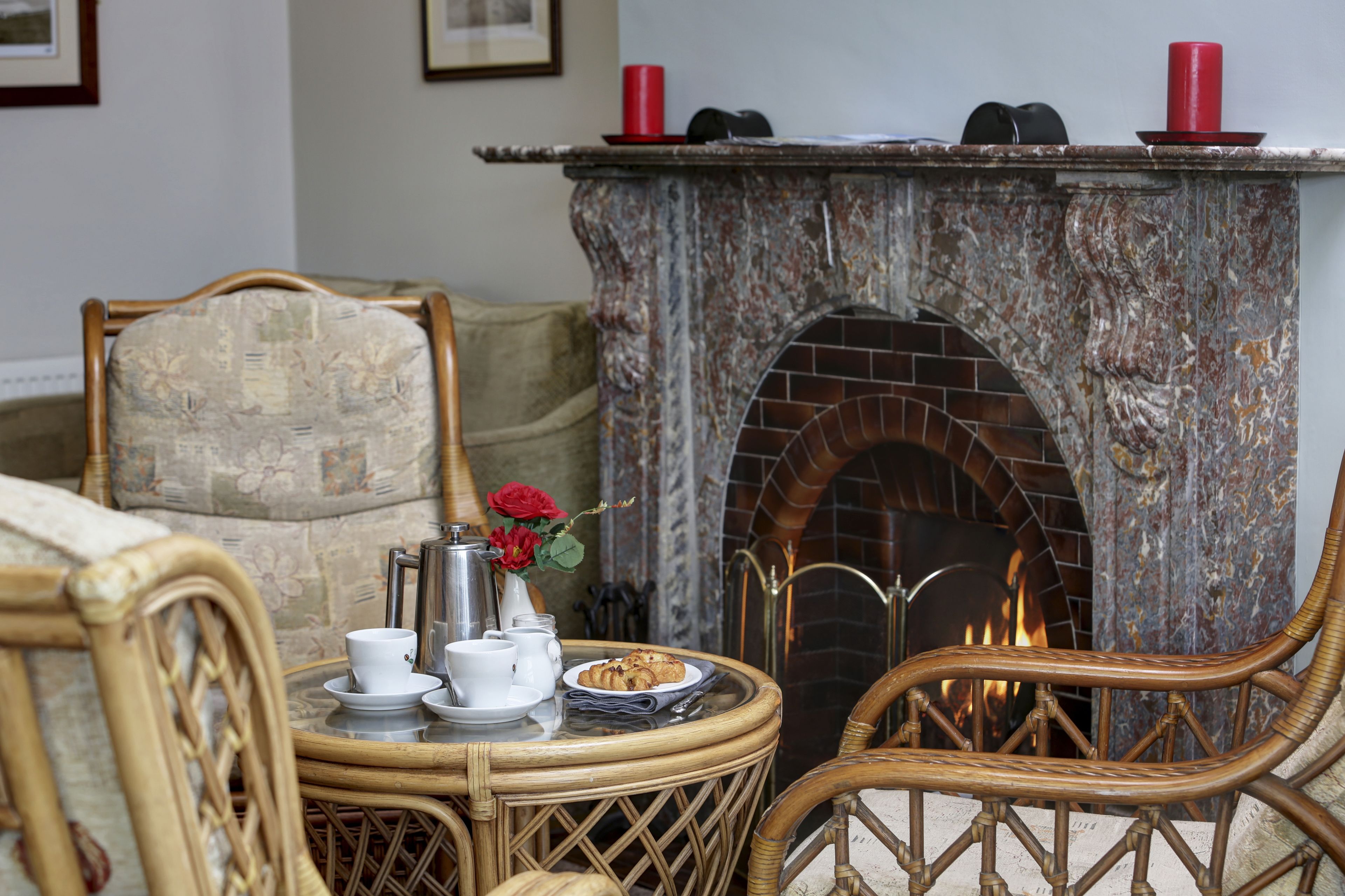 A cozy room with a fireplace, wicker furniture, and a table set with tea cups and a plate of food.