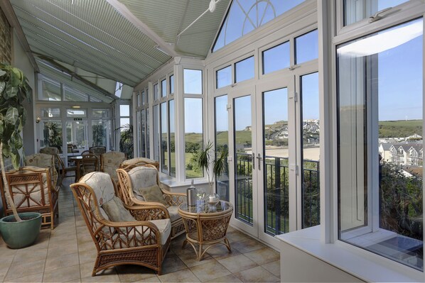 A conservatory with wicker furniture, large windows, and a view of the countryside.