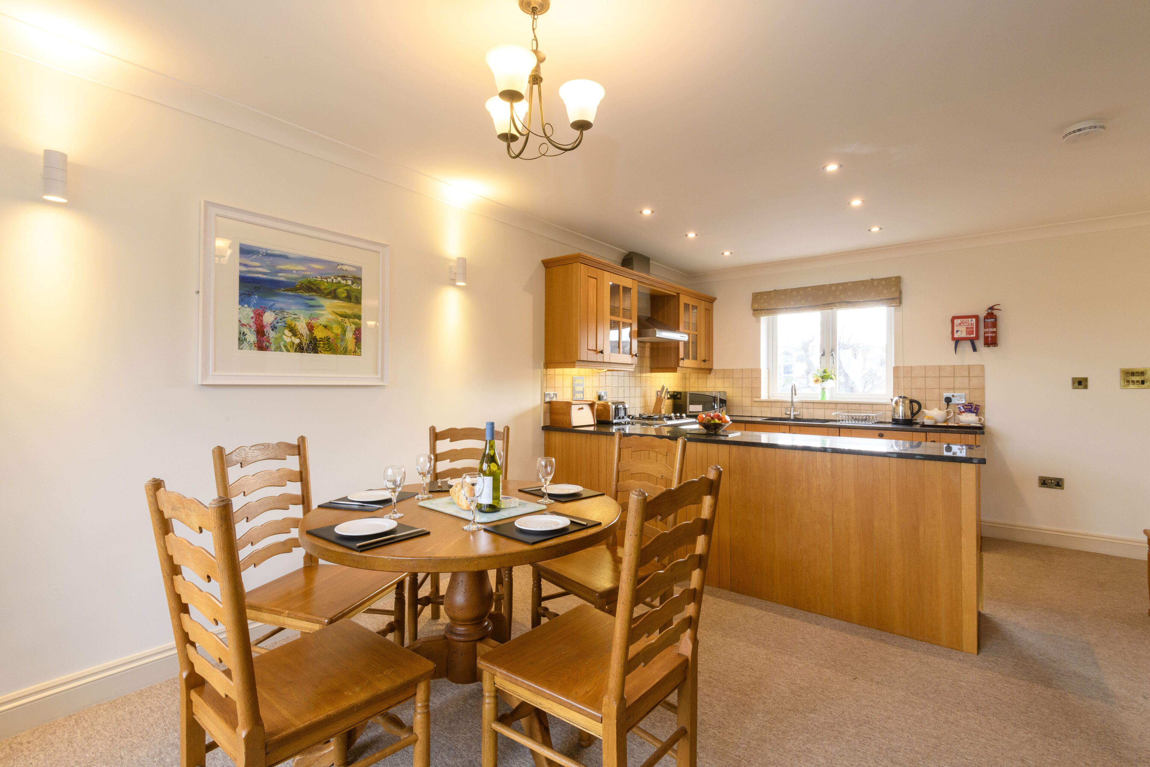 A dining area with a round table, wooden chairs, and a kitchen in the background.