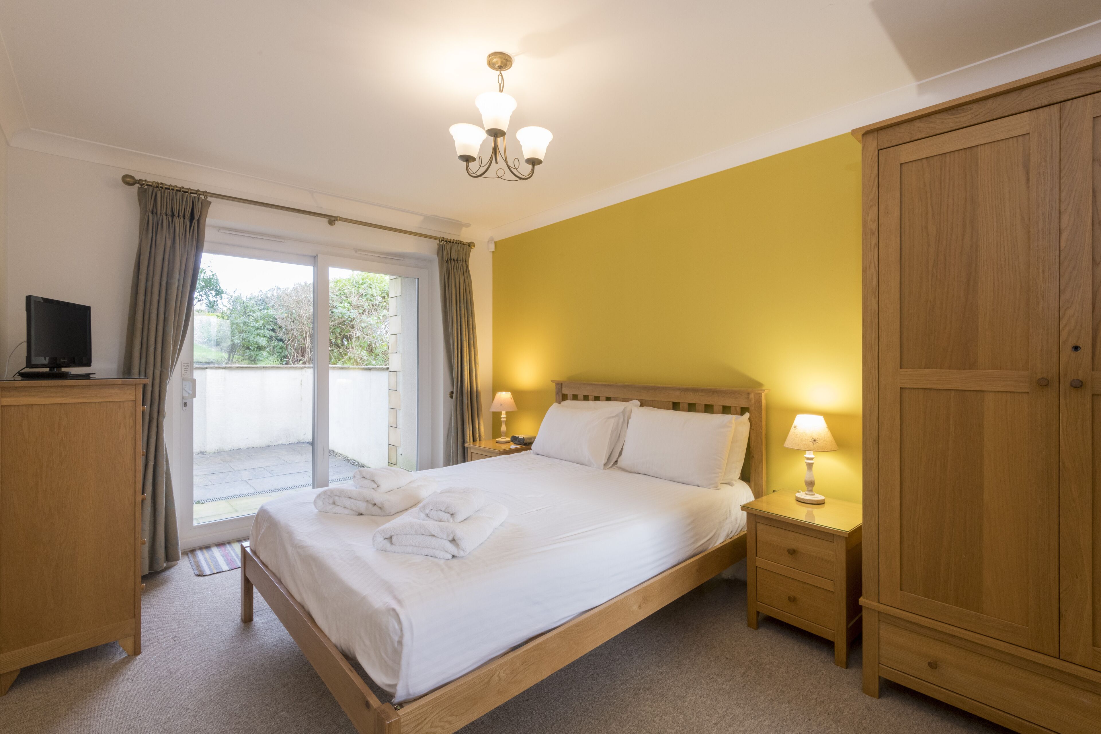 A bedroom with a bed, a wardrobe, a nightstand, a television, and a sliding glass door to the outside.