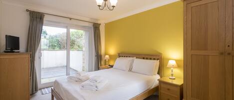 A bedroom with a bed, a wardrobe, a nightstand, a television, and a sliding glass door to the outside.