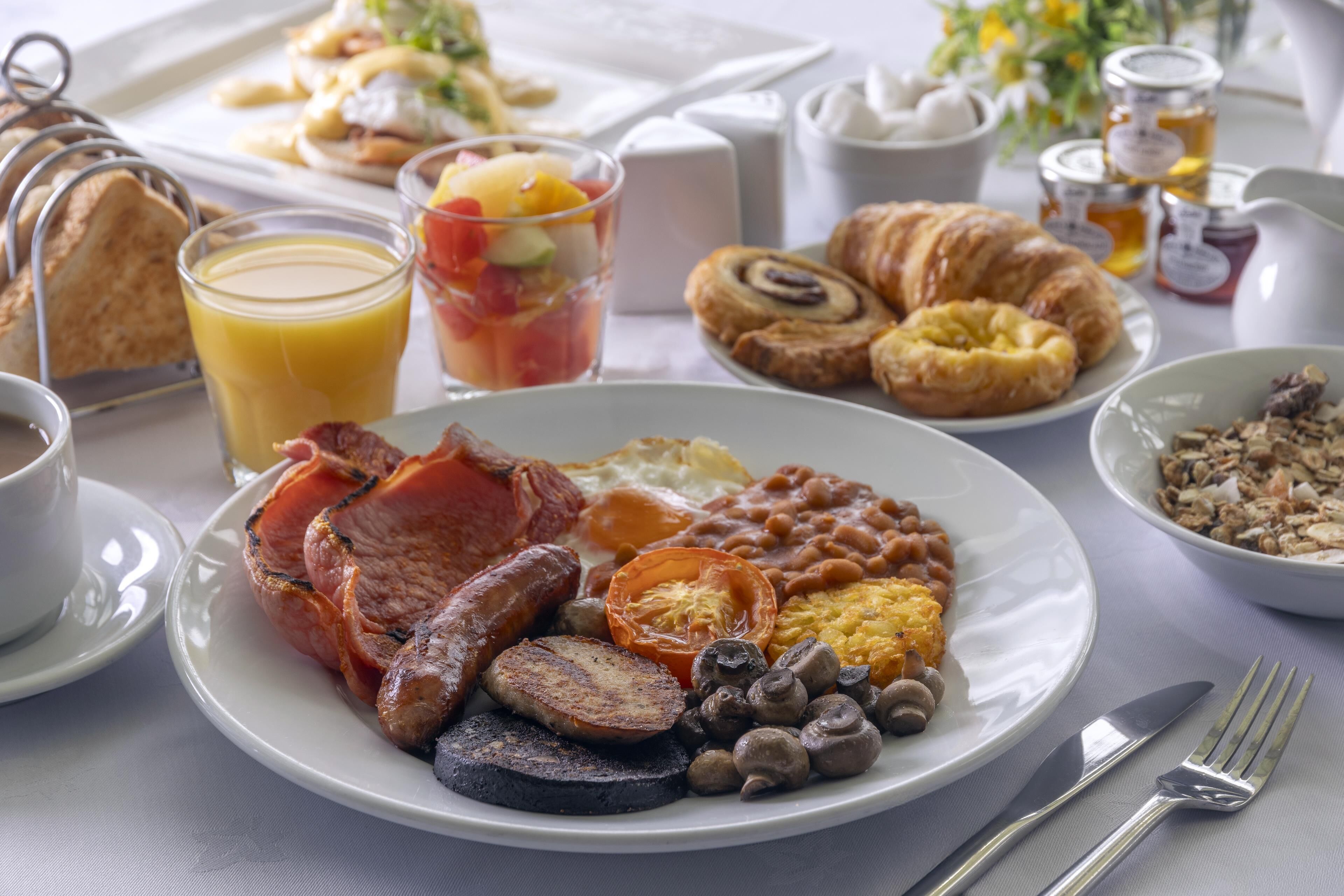 Una mesa de desayuno con diversos alimentos, como huevos, salchichas, champiñones y tostadas.