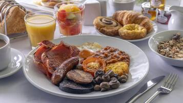 Una mesa de desayuno con diversos alimentos, como huevos, salchichas, champiñones y tostadas.