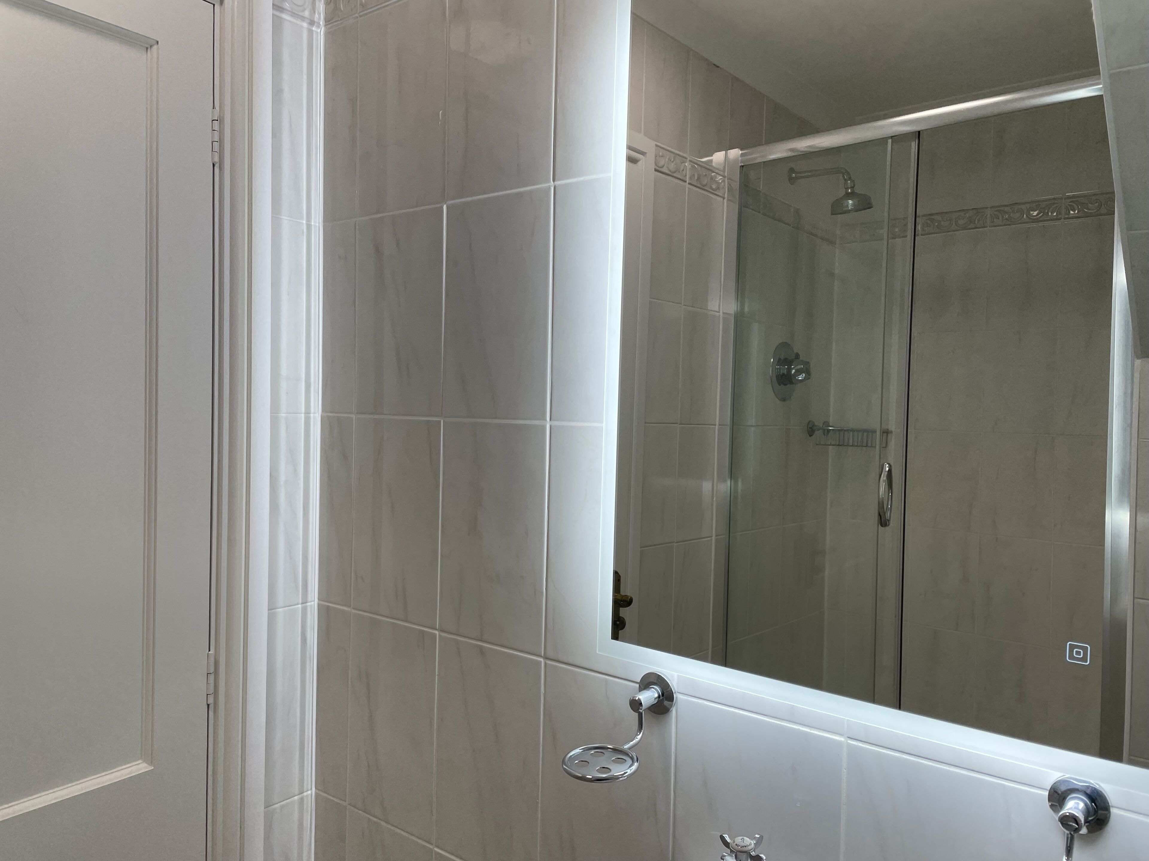 A bathroom with a large mirror, a shower, and a toilet.