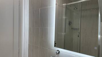 A bathroom with a large mirror, a shower, and a toilet.