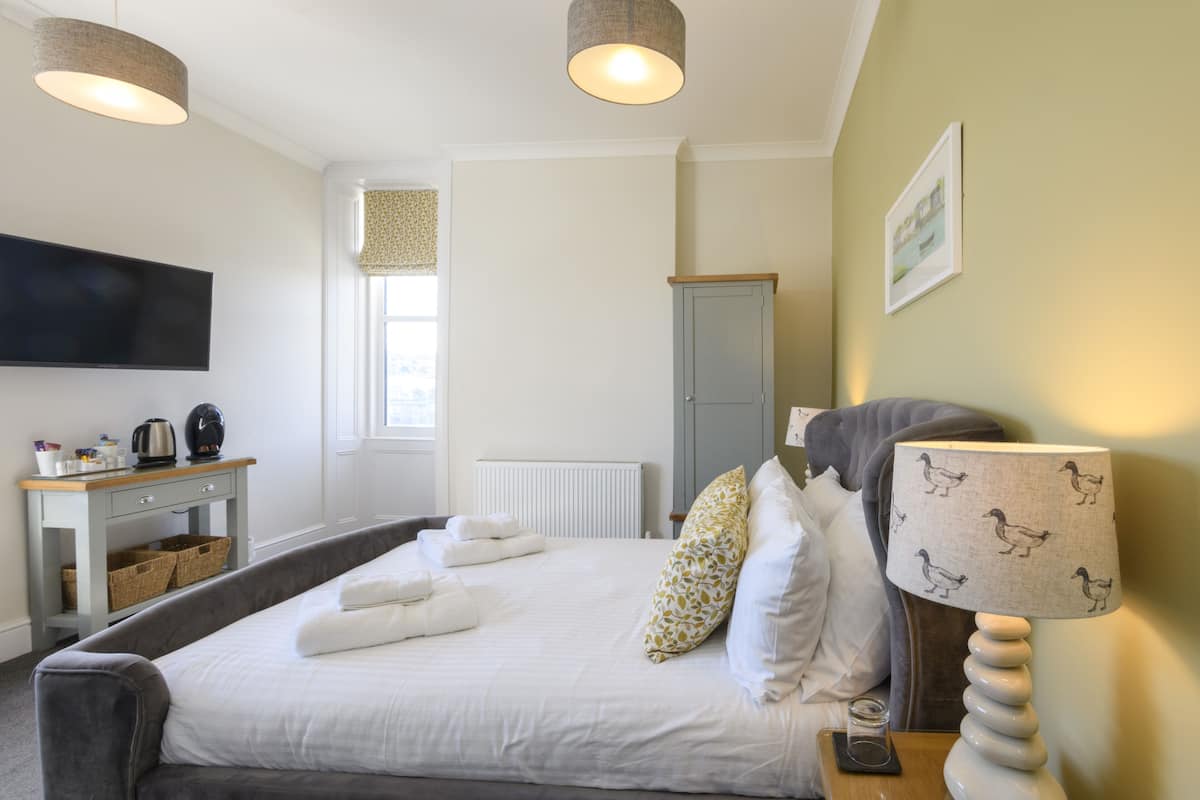 Un dormitorio con cama, mesita de noche, lámpara y televisión en la pared.