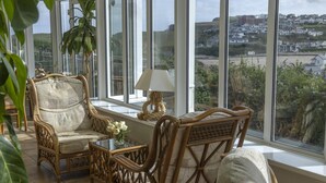 A room with wicker furniture, a table with a lamp, and a view of a coastal town through large windows. - Porth Veor Manor, Sure Hotel Collection by Best Western (Newquay)