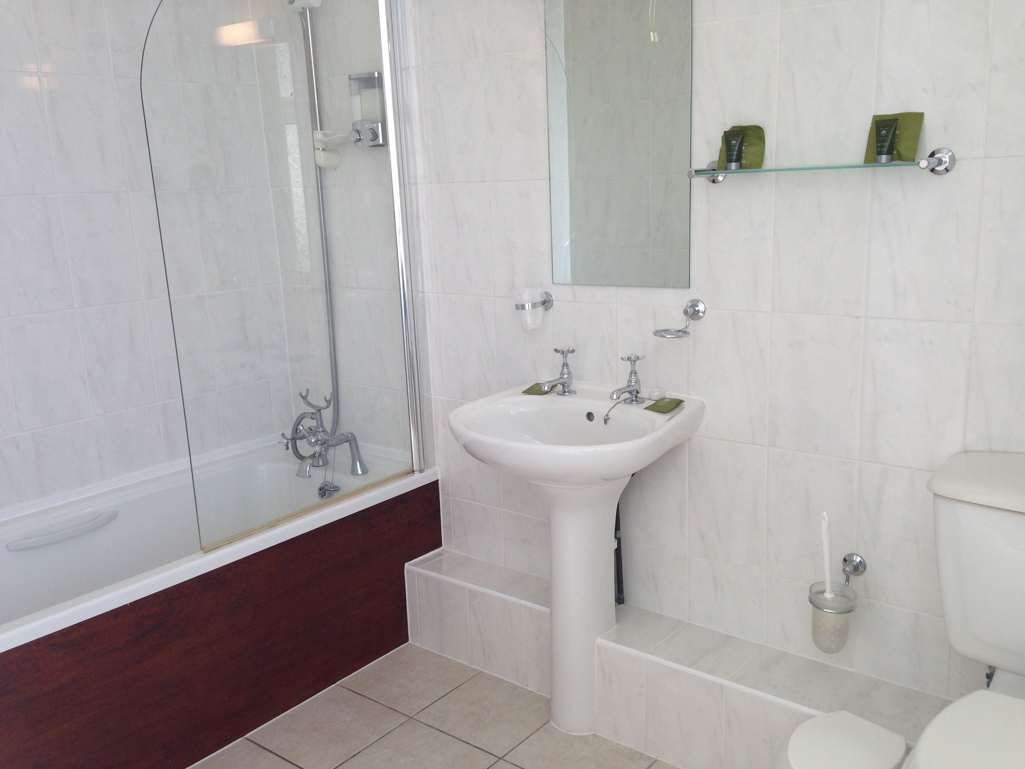 A modern bathroom with a glass-enclosed shower, a white sink with two faucets, and a toilet.