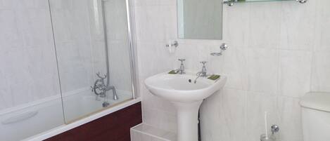 A modern bathroom with a glass-enclosed shower, a white sink with two faucets, and a toilet.