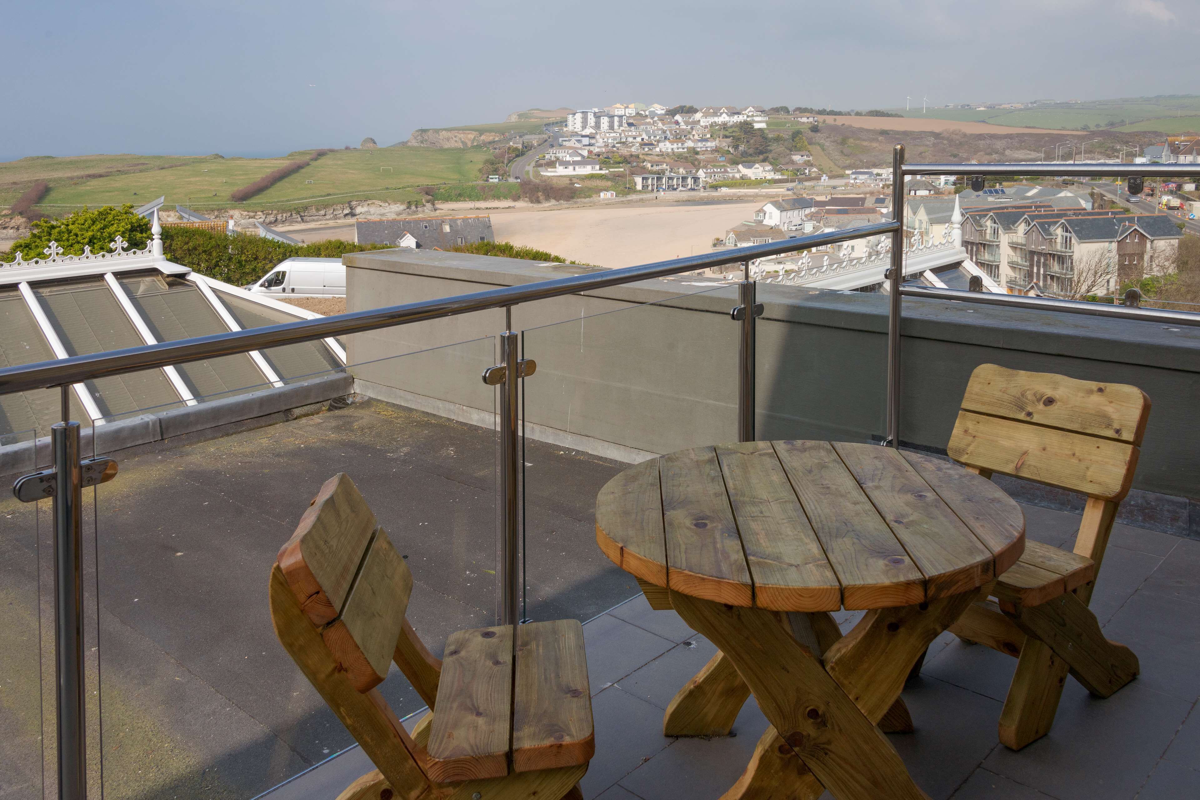 Un balcón con mesa y sillas de madera, con vistas a un pueblo costero con edificios y una playa.