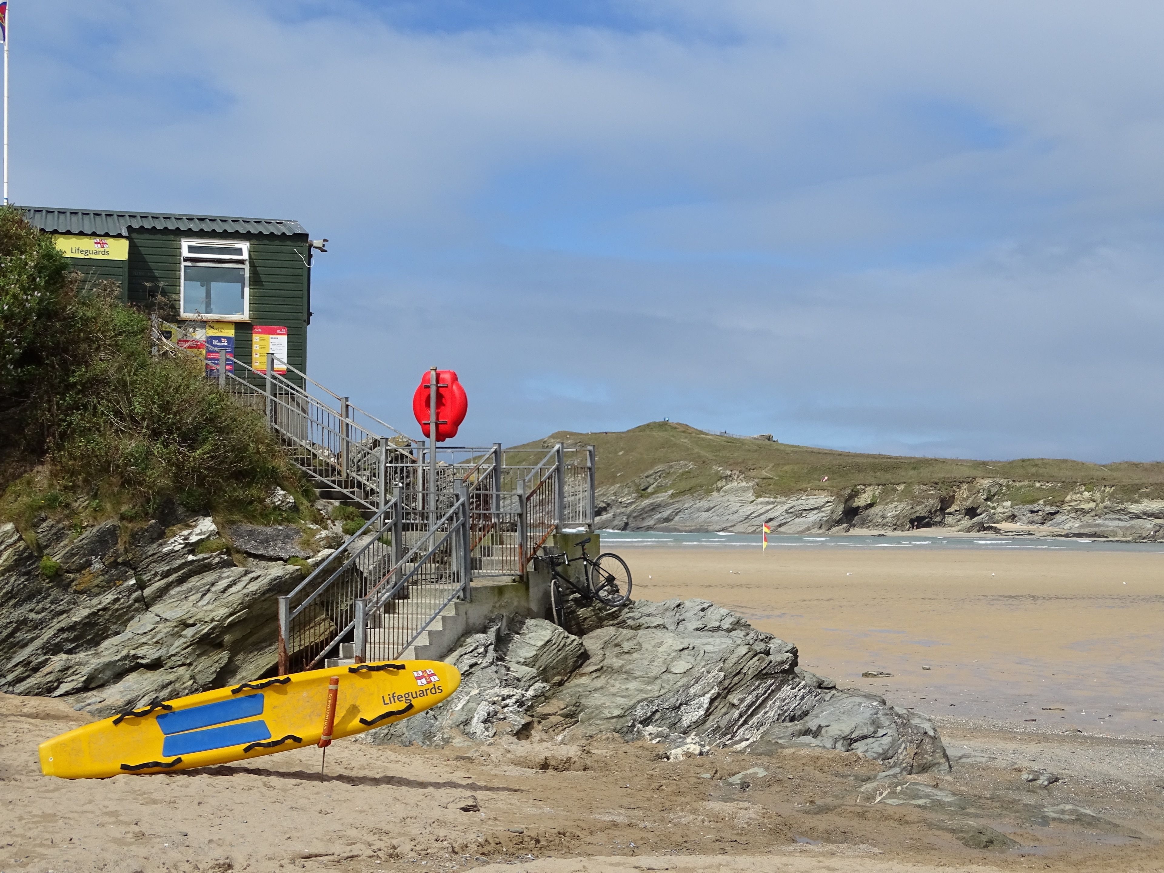 Ein Rettungsturm mit Rettungsstuhl und einem gelben Rettungsboot an einem felsigen Strand.