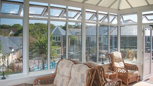 A conservatory with wicker furniture and large windows offering a view of a swimming pool and houses. - Porth Veor Manor, Sure Hotel Collection by Best Western (Newquay)