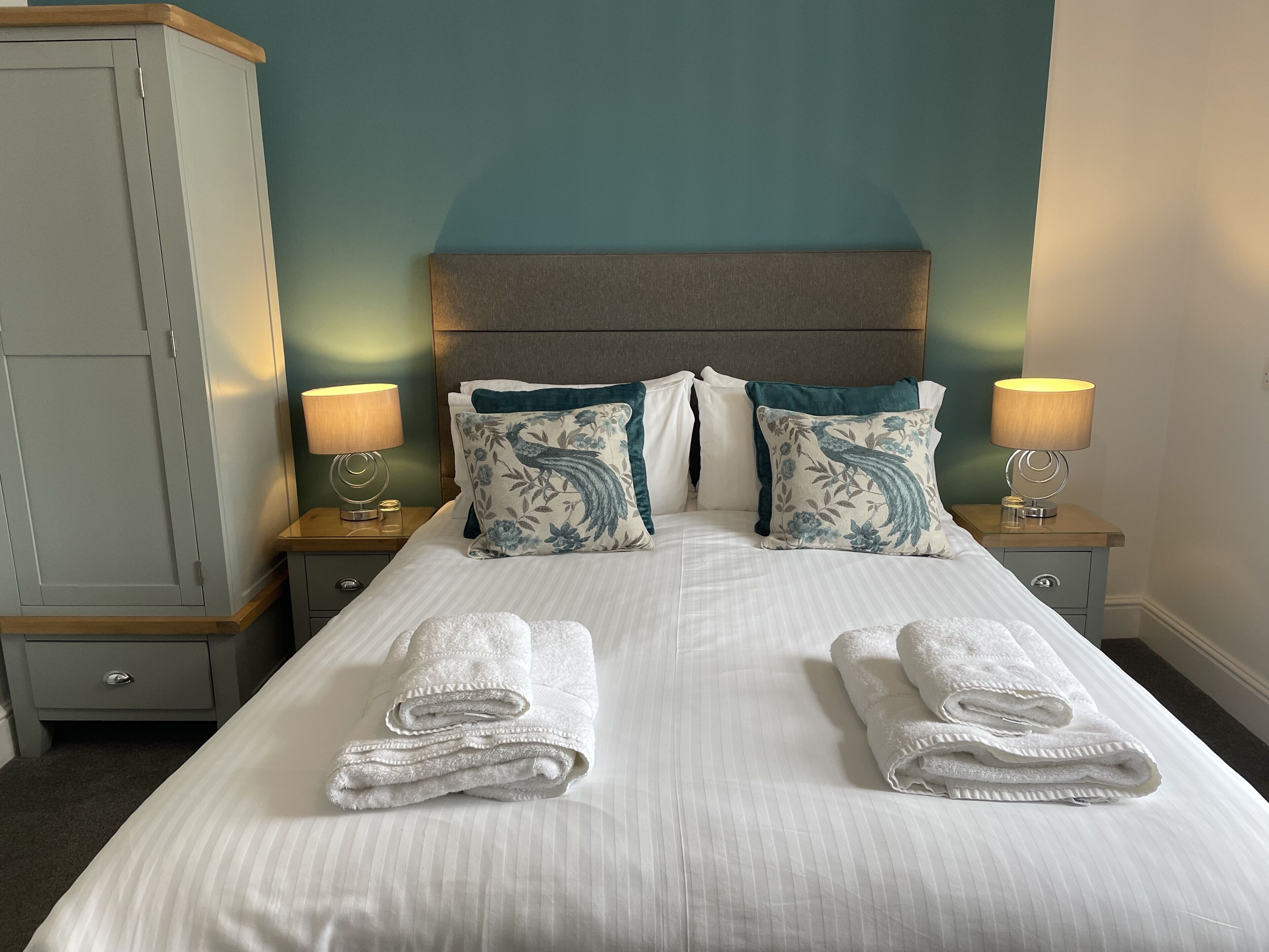 A neatly made bed with two pillows, two bedside tables with lamps, and a wardrobe.
