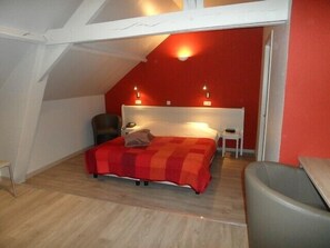 A bedroom with a sloped ceiling, a bed with a red and orange bedspread, two bedside lamps, a chair, and a small table. - B&B Ter Gracht (Wevelgem)