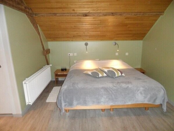 Un dormitorio con techo de madera, una cama con manta gris, dos lámparas de noche y una mesita de noche de madera.