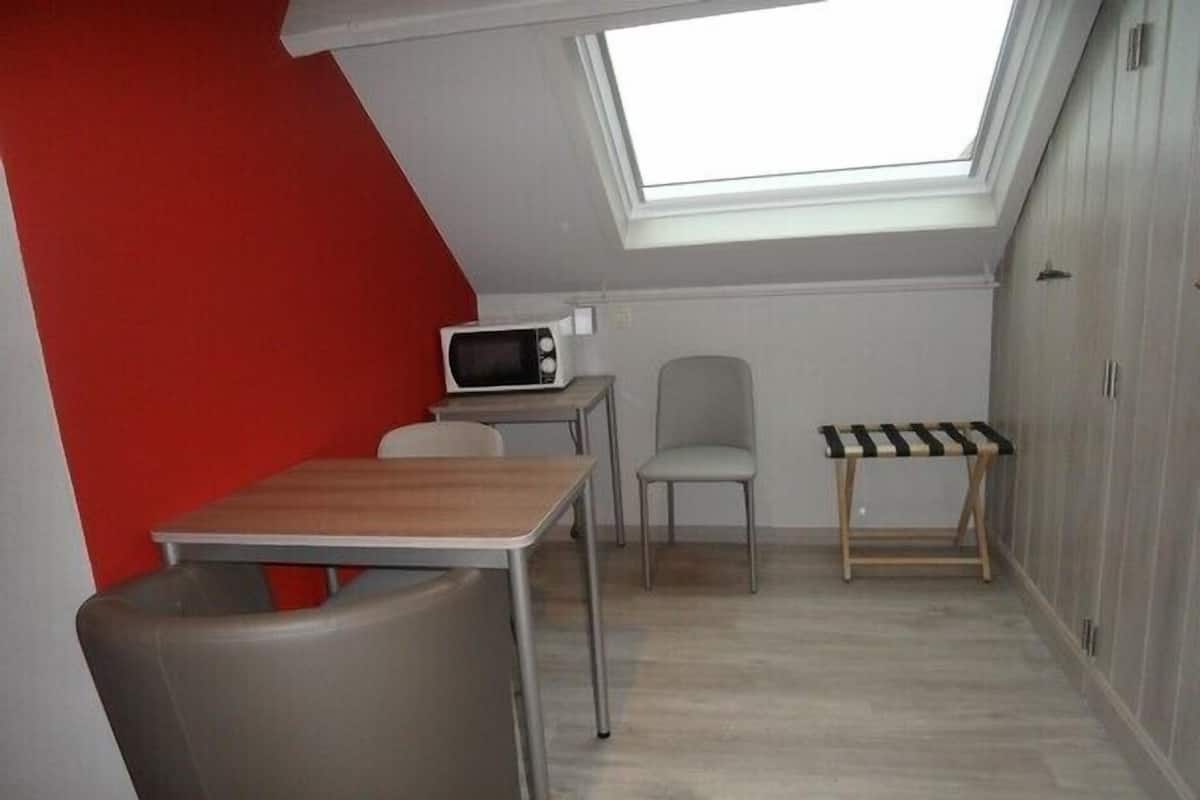 Una habitación pequeña y funcional con tragaluz, microondas, mesa, silla y banco.