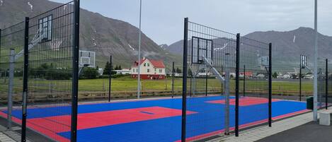 Una cancha de baloncesto al aire libre con superficie roja y azul, rodeada por una valla metálica.