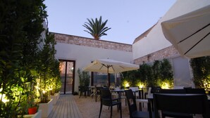 An outdoor patio area with tables and chairs, surrounded by plants and a stone wall. - LoL Hostel Siracusa (Syracuse)