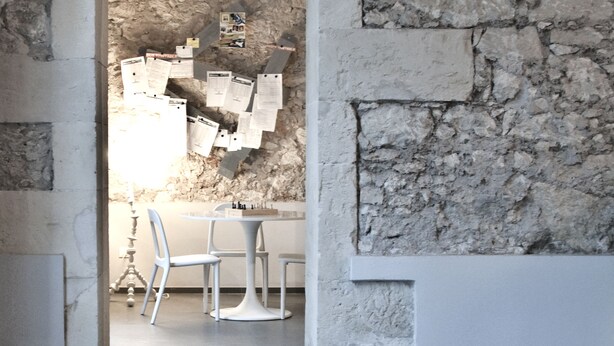 An interior with a stone wall, a white archway, and a dining area with chairs and a table. - LoL Hostel Siracusa (Syracuse)
