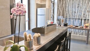 A modern kitchen with a long countertop, a refrigerator, and a dining area with chairs. - LoL Hostel Siracusa (Syracuse)