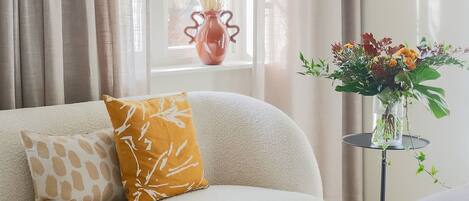 A living room with a sofa, a small table with a vase of flowers, and a window with curtains.