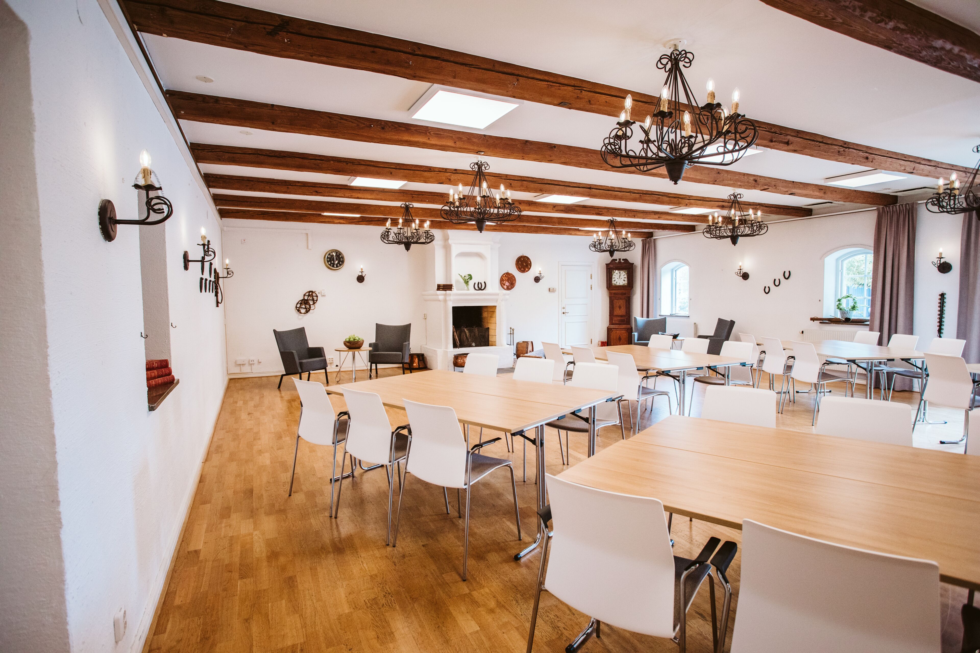 A conference room with wooden beams, chandeliers, white chairs, and a long table.