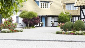 Um edifício tradicional com área de recepção, pátio de paralelepípedos e canteiros de flores bem cuidados.